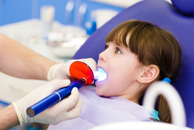 little girl with open mouth receiving dental filling drying proc