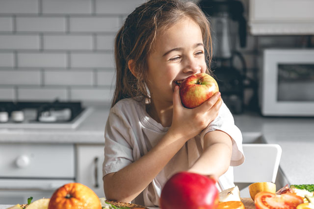 Funny little girl appetizingly eats apples in the kitchen, health and nutrition concept.